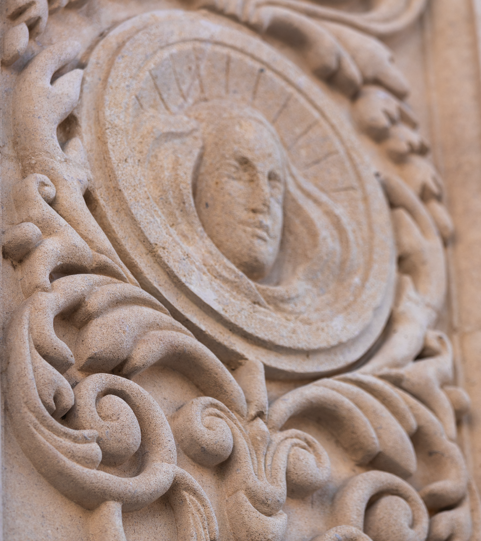 Close-up of an ornate stone carving featuring a face surrounded by intricate scrollwork