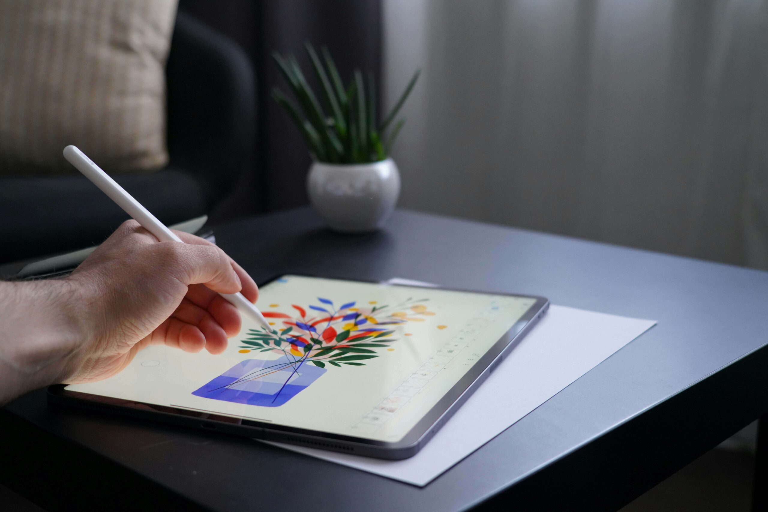 Hand using stylus to create digital illustration of colorful flowers in a vase on a tablet