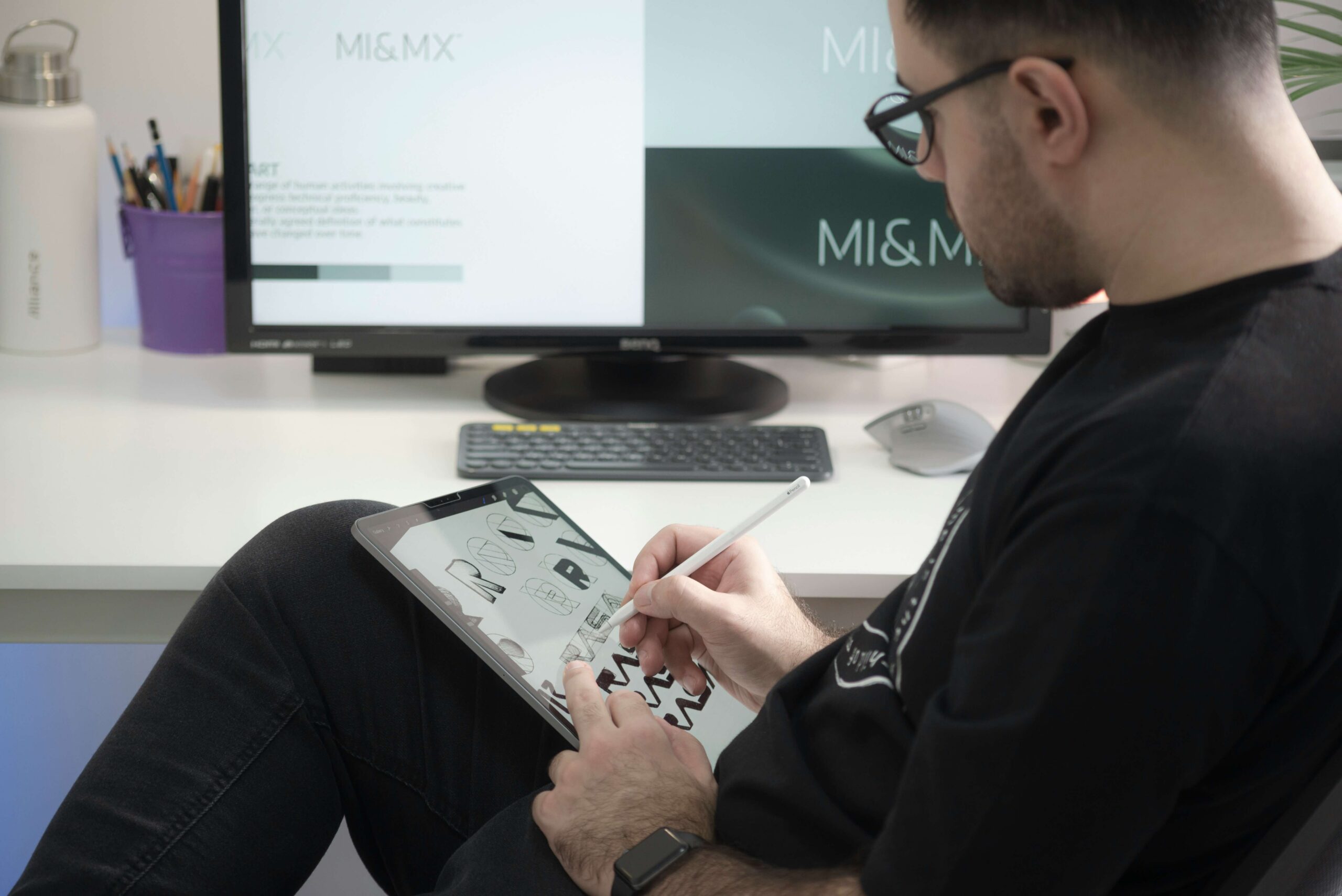 Person designing lettering on a tablet with stylus in front of a computer screen showing brand strategy