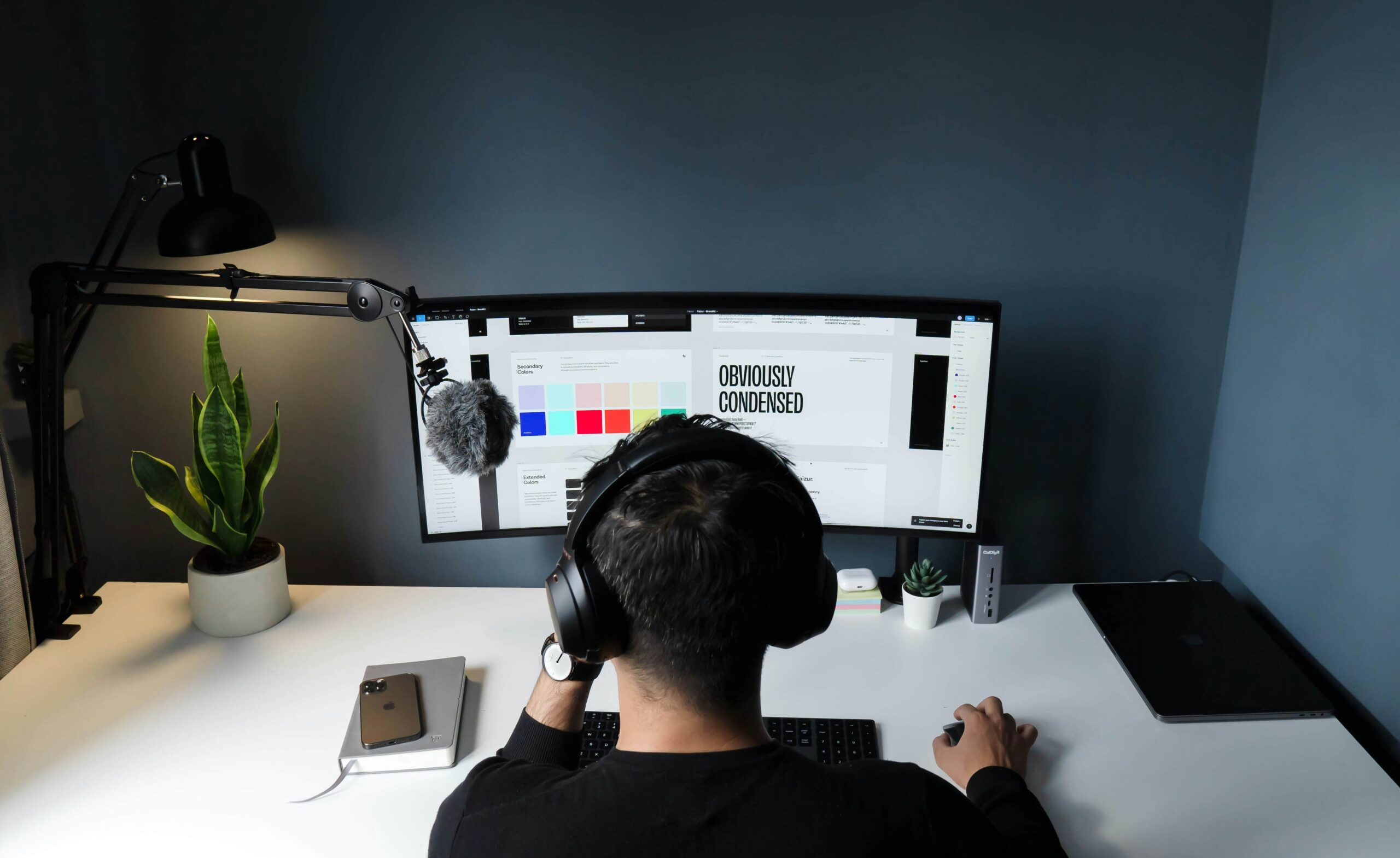 Person working on graphic design on a wide curved monitor with headphones on
