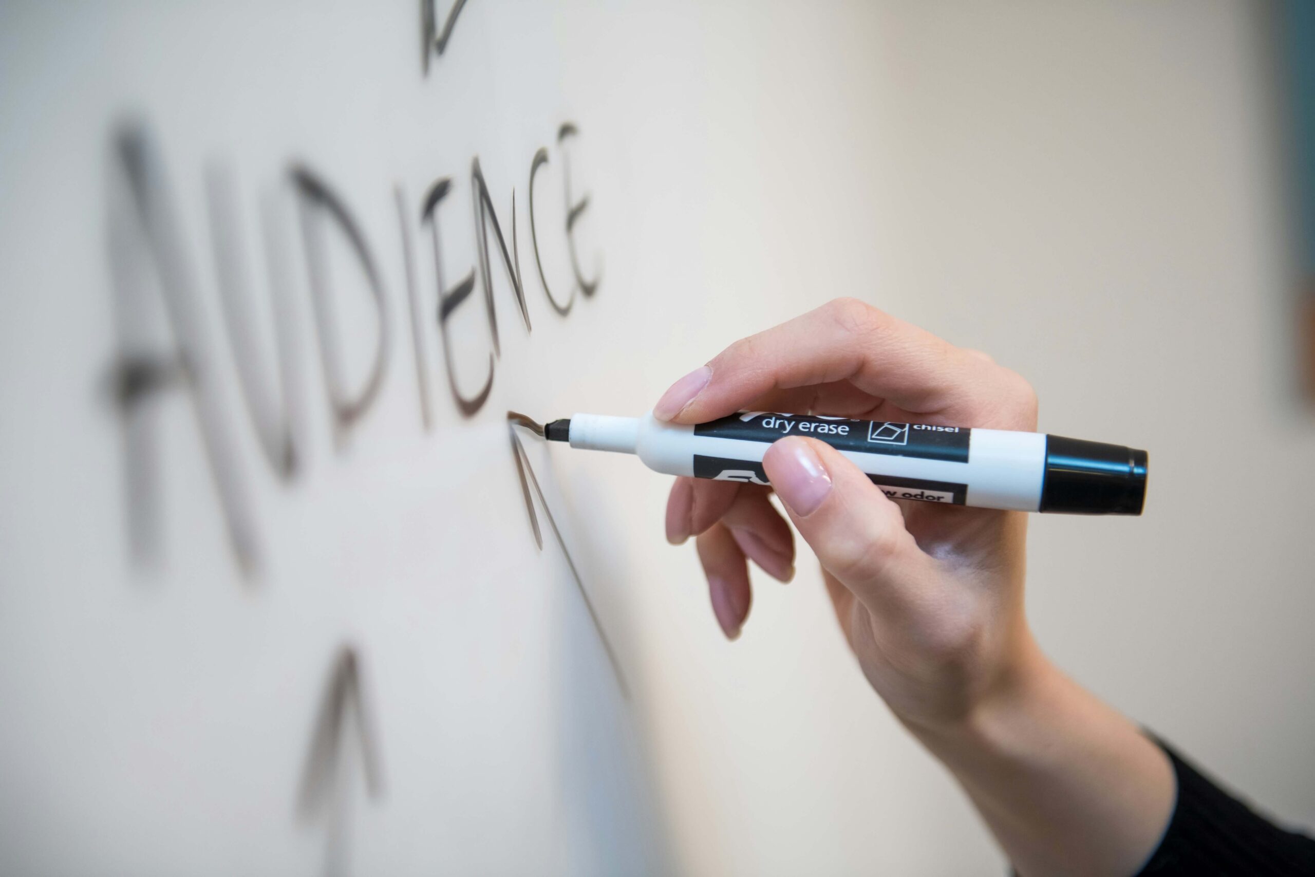 Hand writing 'AUDIENCE' with dry erase marker on whiteboard