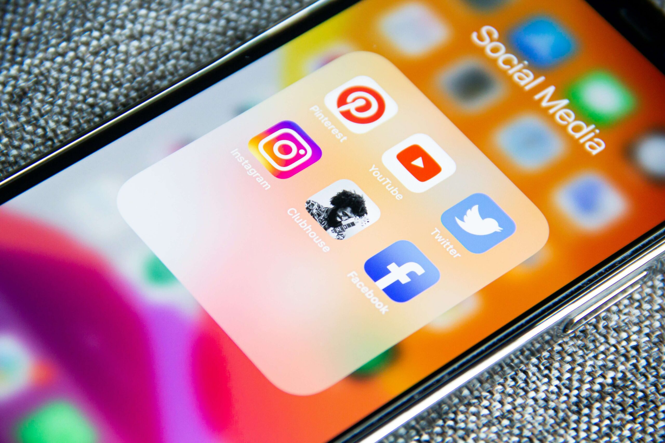 Smartphone screen showing social media apps folder with Instagram, Pinterest, YouTube, Twitter, Facebook, and Clubhouse