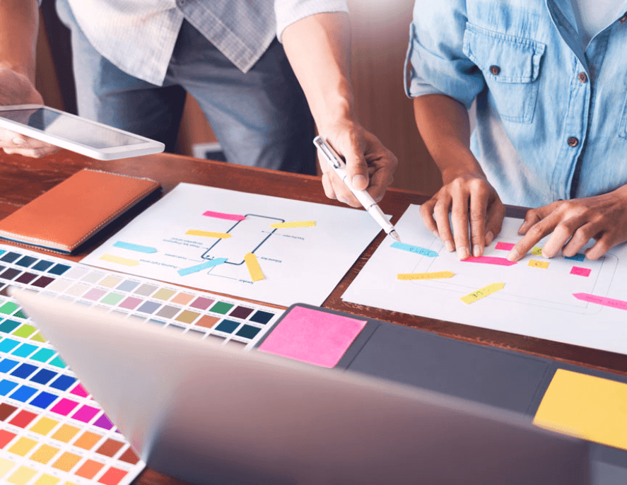 Two people working on website design with color swatches and layout sketches
