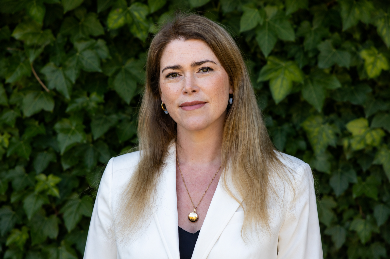 Portrait of Kate Bygrave in white blazer with greenery background