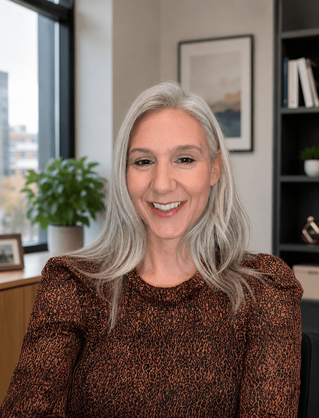 Smiling woman with gray hair wearing a patterned brown top in an office setting