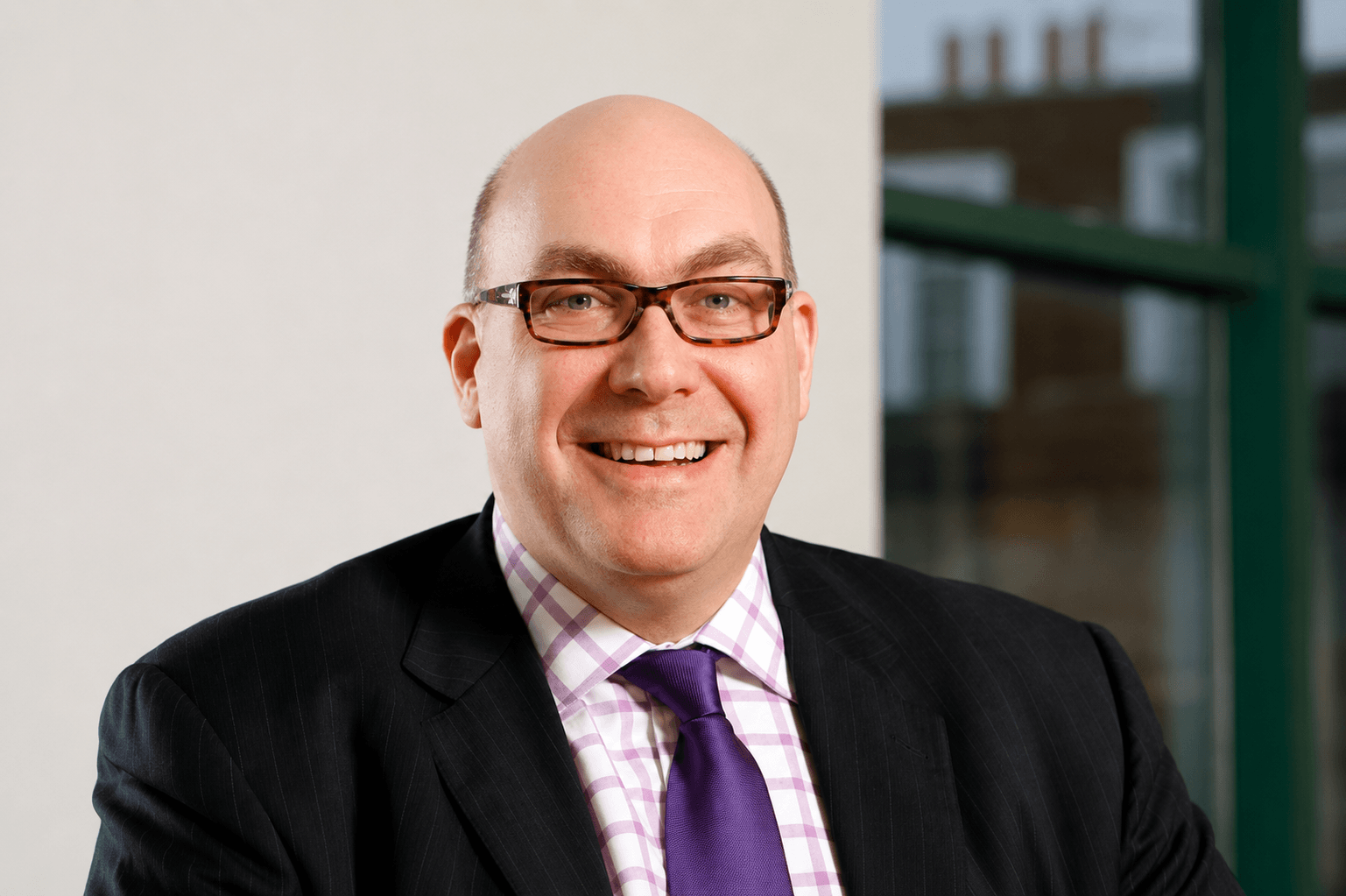 Smiling man wearing glasses, a checkered shirt, purple tie, and dark suit jacket