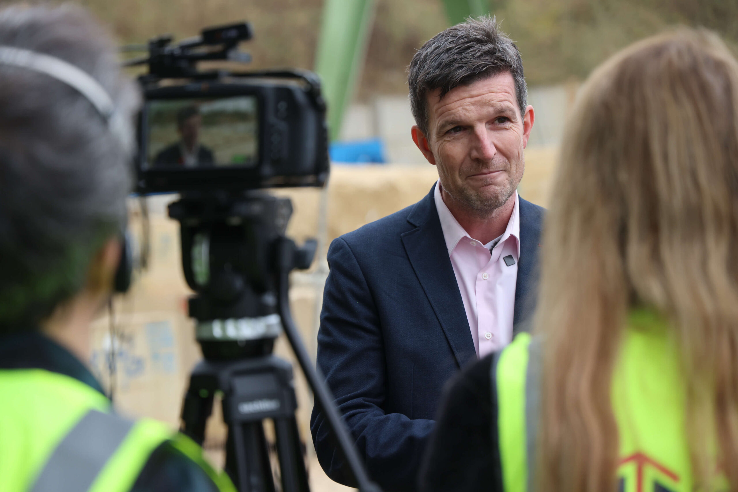 Man in suit being interviewed on camera at construction site