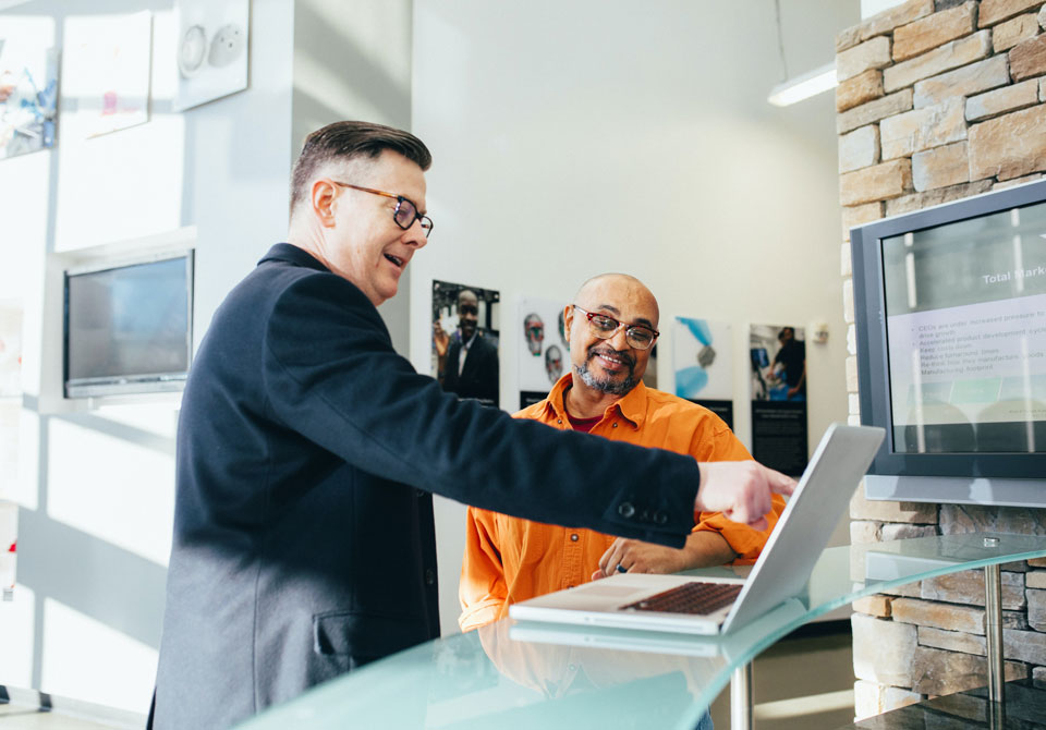 Two men discussing content on a laptop at a modern office counter