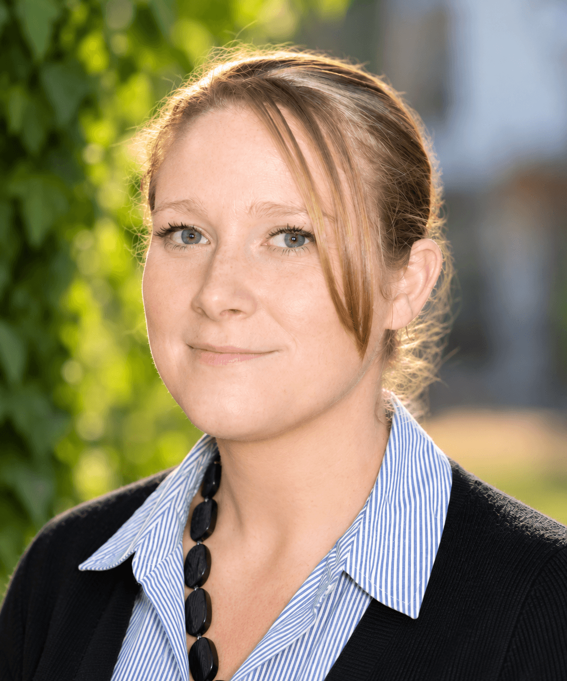 Portrait of a woman with light hair pulled back, wearing a striped shirt and black cardigan