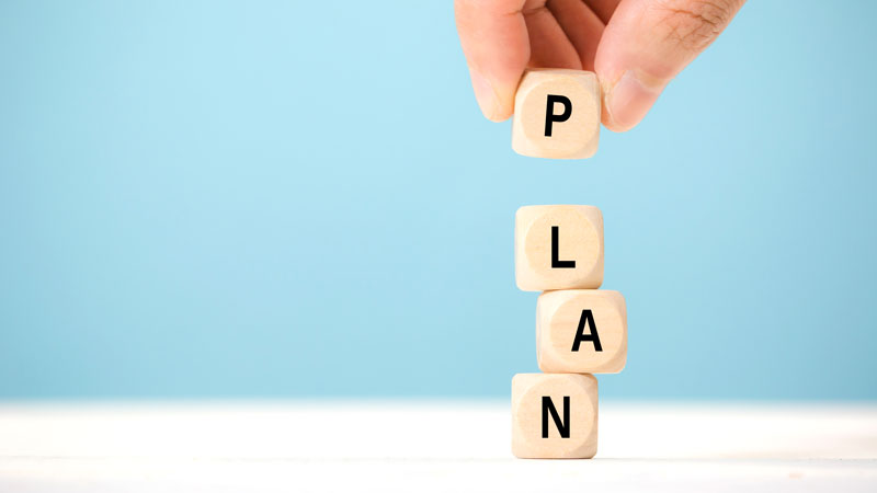 Hand stacking wooden blocks spelling the word PLAN