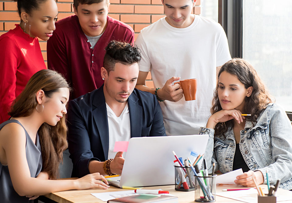 Group of young adults working together around a laptop in a casual setting