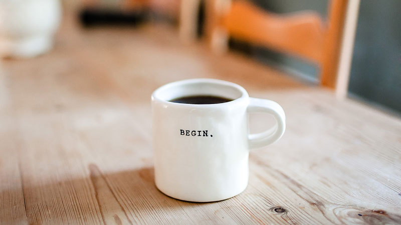 White coffee mug with the word BEGIN on a wooden table